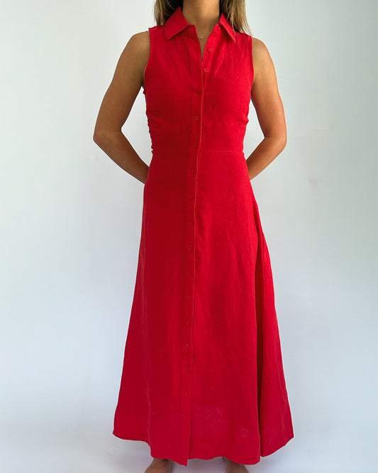 A woman wearing a sleeveless, bright red dress with a buttoned front and collared neckline stands against a white background, exuding elegance.
