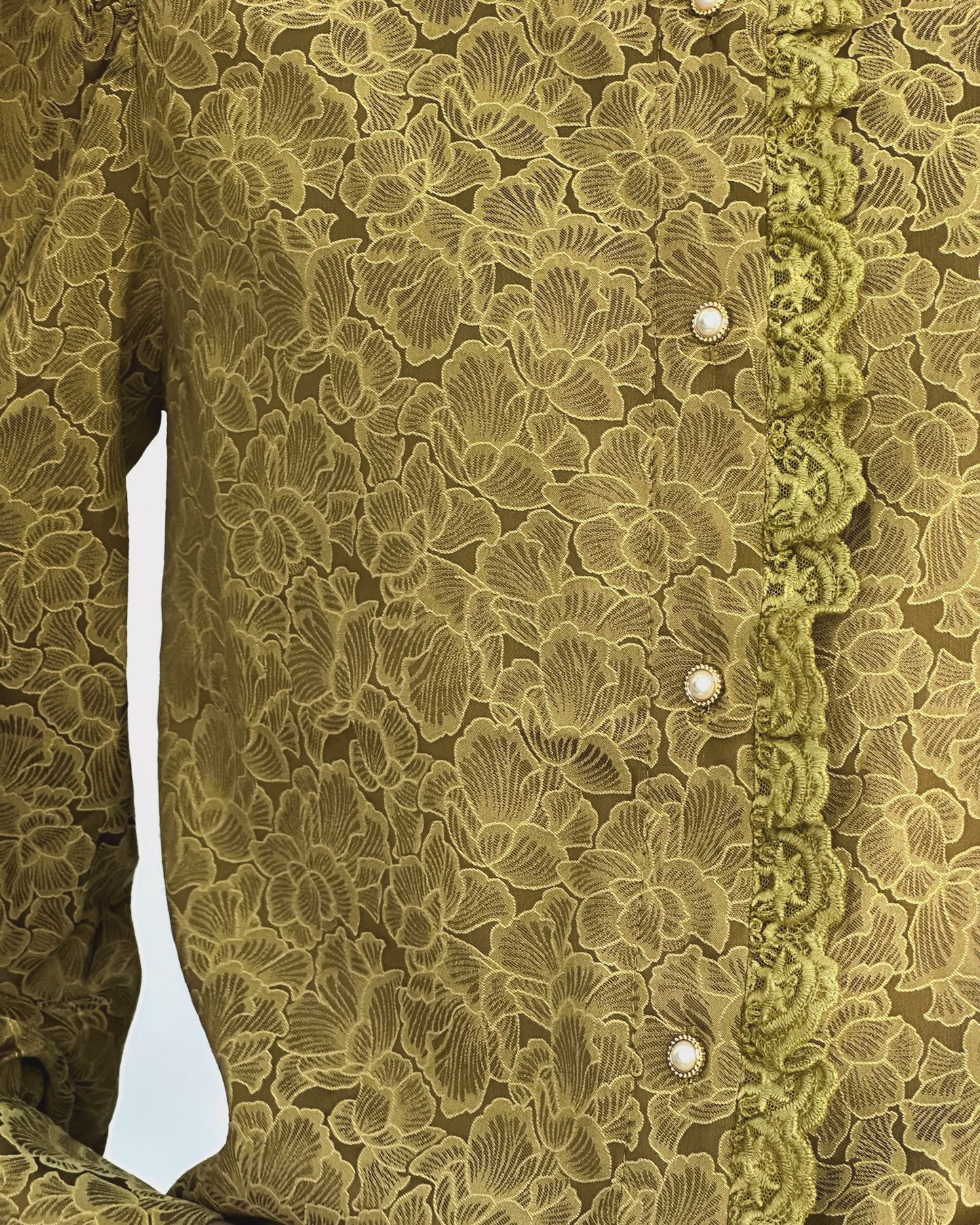 Person wearing a vintage-style green lace blouse with puffed sleeves and pearl buttons, paired with white pants. The look is elegant and classic.