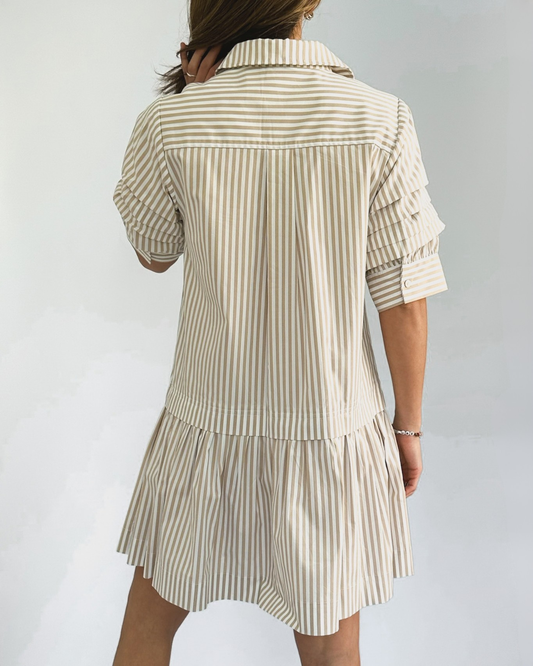 A person wearing a beige and white vertically striped shirtdress with ruffled sleeves. The dress has a collared neckline and falls above the knee.