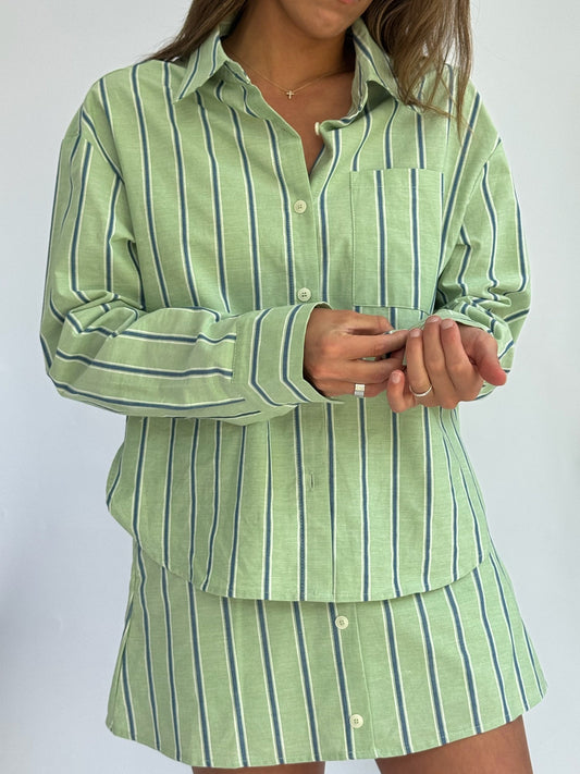 A person wears a light green, button-up shirt and matching skirt with vertical blue and white stripes, conveying a casual and fresh look.