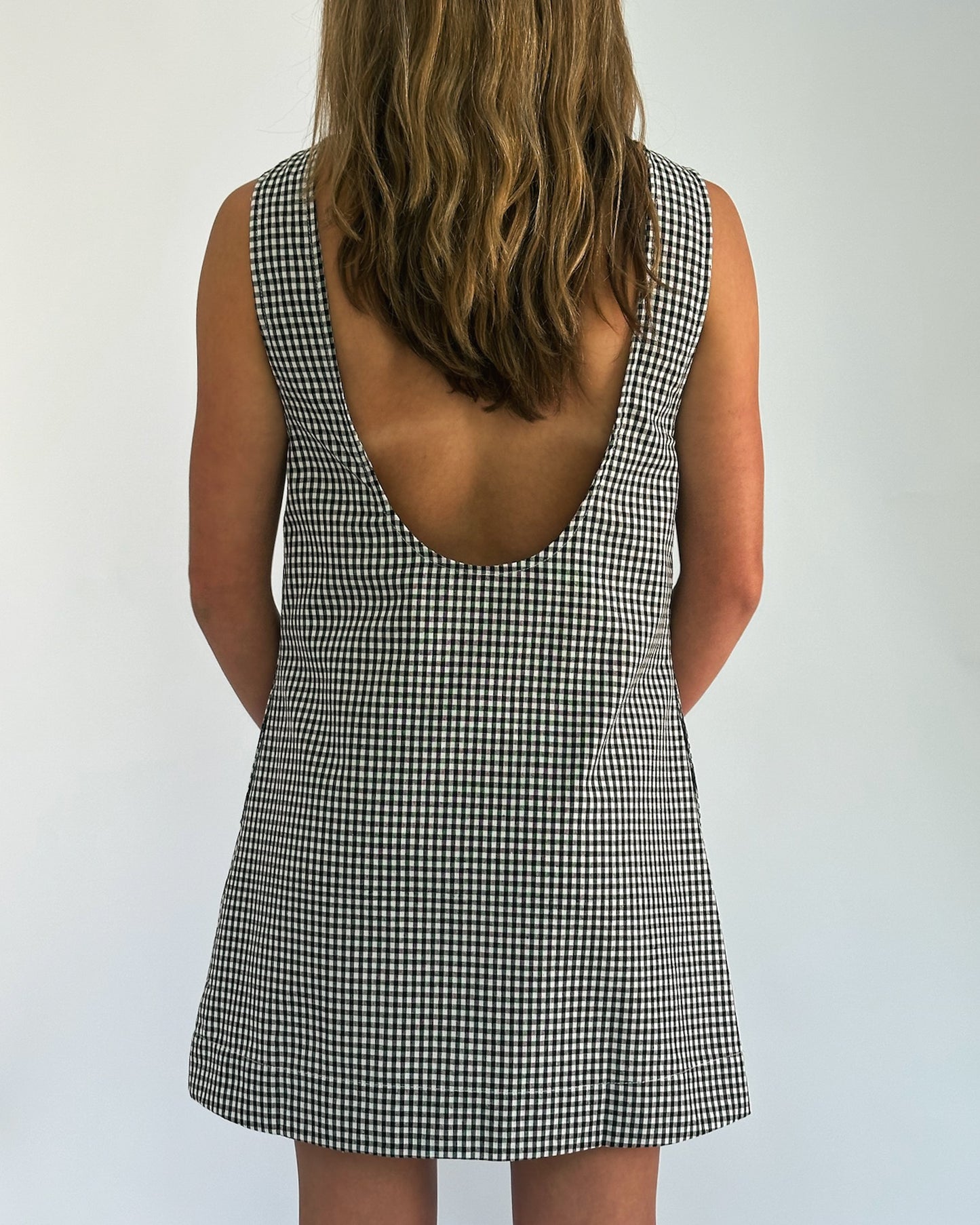 A woman with wavy blonde hair wearing a black-and-white checkered dress with a deep open back. She is facing away against a plain background.