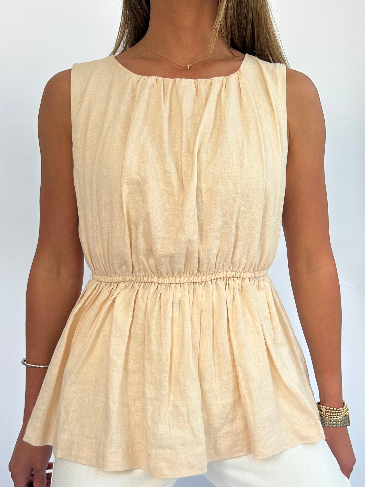 A person wearing a sleeveless, peach-colored, gathered top. The outfit features a cinched waist and is paired with light-colored pants, conveying a casual and elegant style.