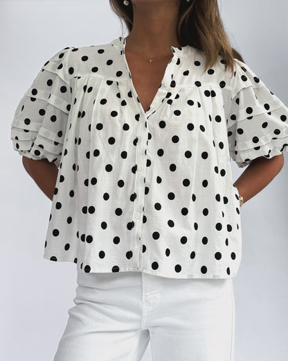 White blouse with black polka dots worn by a person on a white background