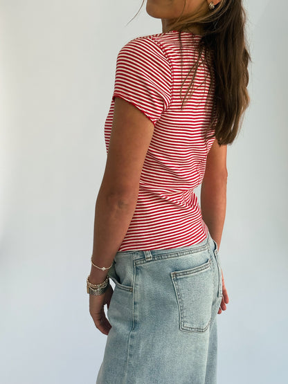 A person in a red and white striped shirt and light blue denim skirt is standing sideways against a plain background, exuding a casual and relaxed vibe.