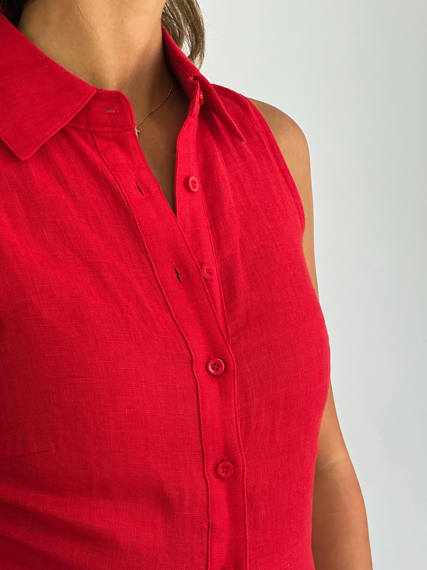 A person wearing a sleeveless, button-up red shirt with a collar. The fabric appears soft and the overall tone is vibrant and casual.