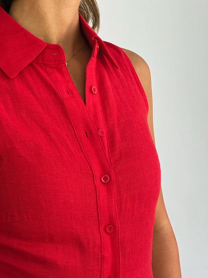 A person wearing a sleeveless, button-up red shirt with a collar. The fabric appears soft and the overall tone is vibrant and casual.