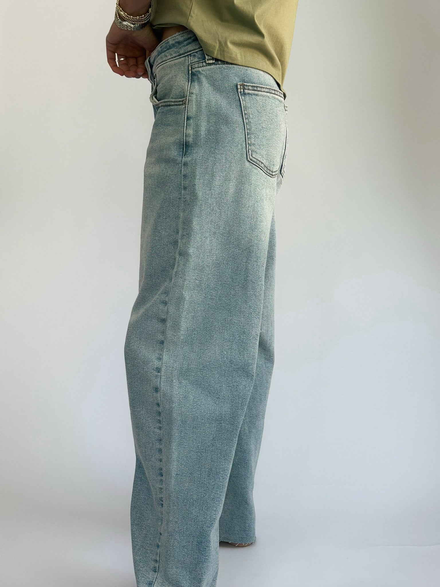 Person wearing light blue, loose-fitting jeans paired with a light green shirt. The jeans have a back pocket, and the person is standing against a plain background.