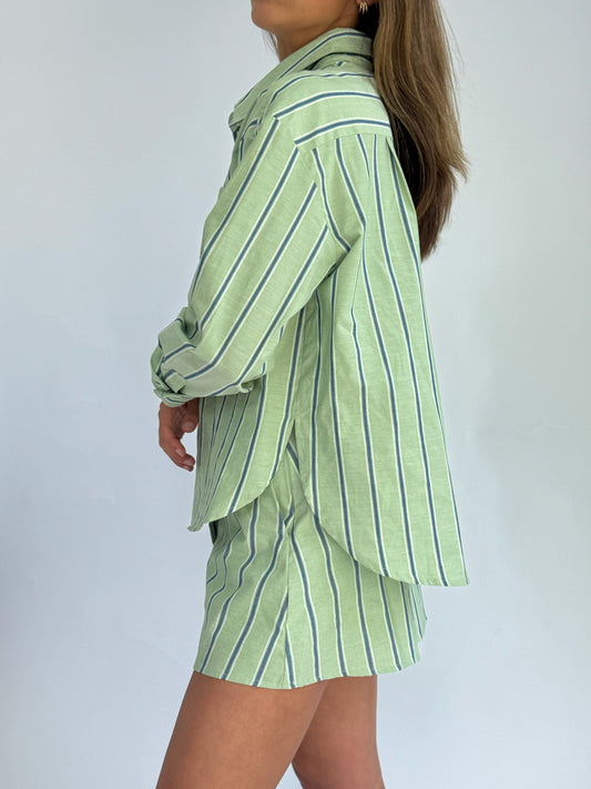 A person wears a light green, button-up shirt and matching skirt with vertical blue and white stripes, conveying a casual and fresh look.