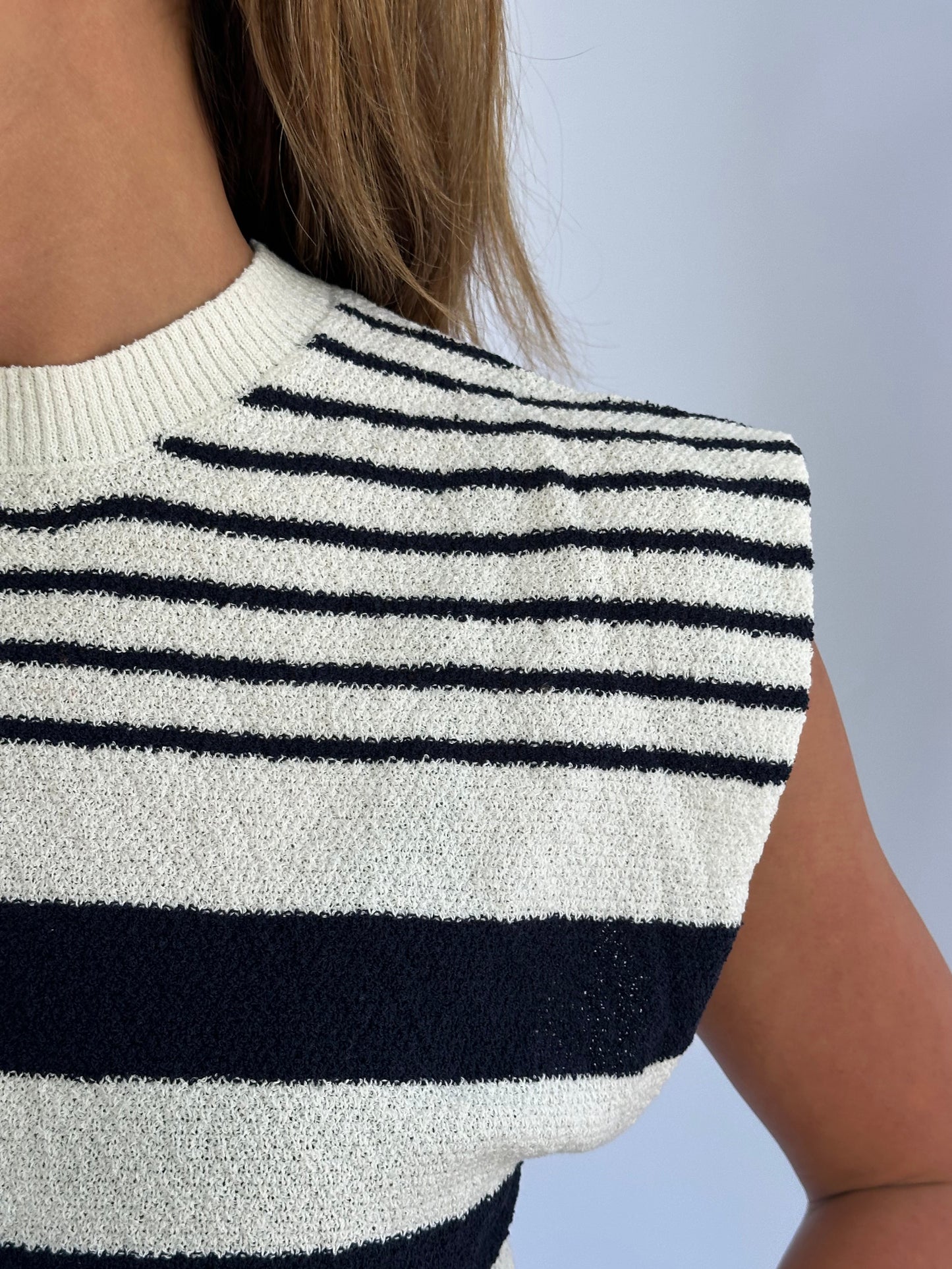 Close-up of a person's shoulder wearing a sleeveless top with navy and white horizontal stripes. The texture is terry towel like matieral.