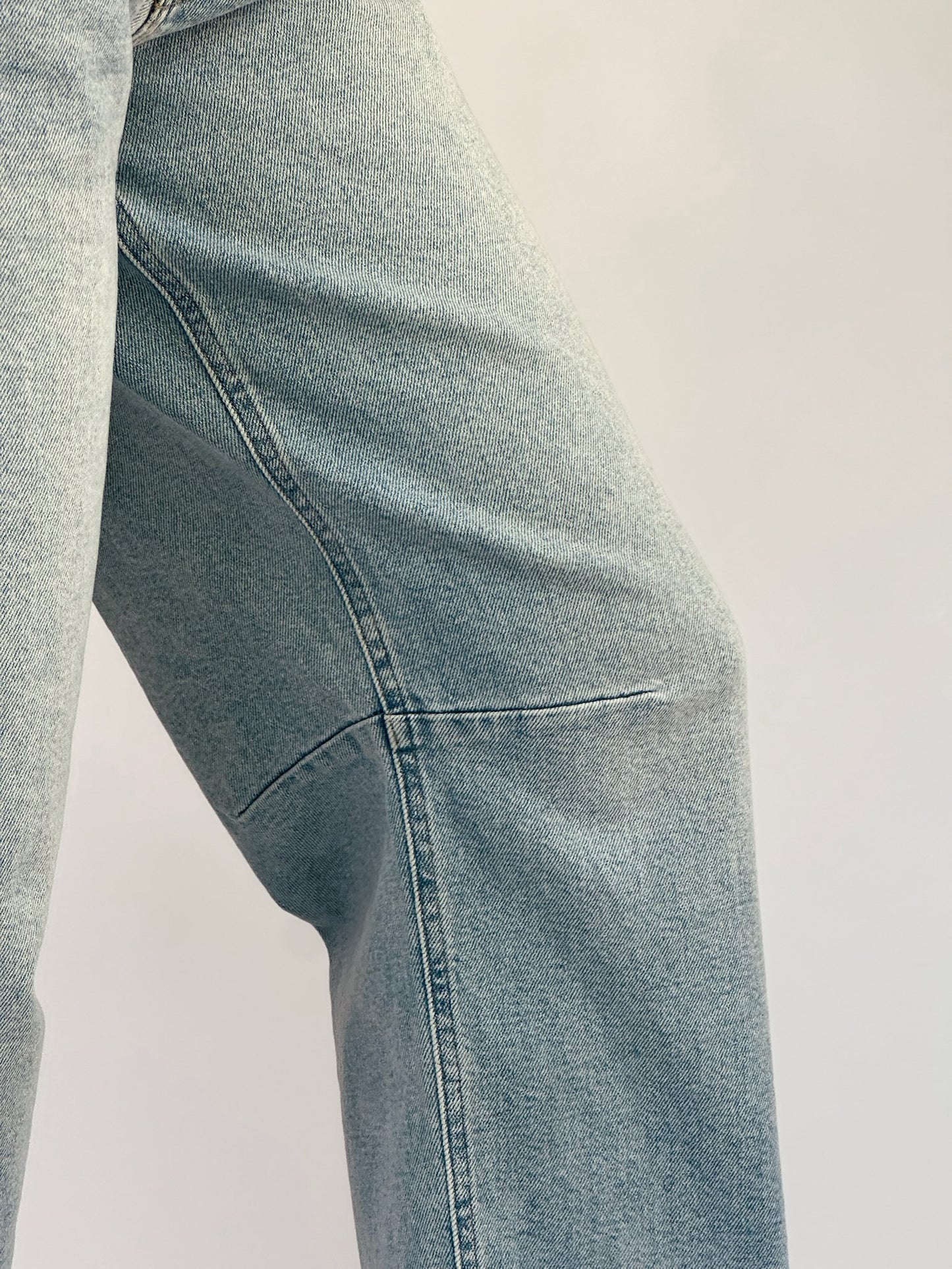 Close-up of a person wearing light blue denim jeans with visible stitching and texture, against a neutral background, conveying a casual tone.