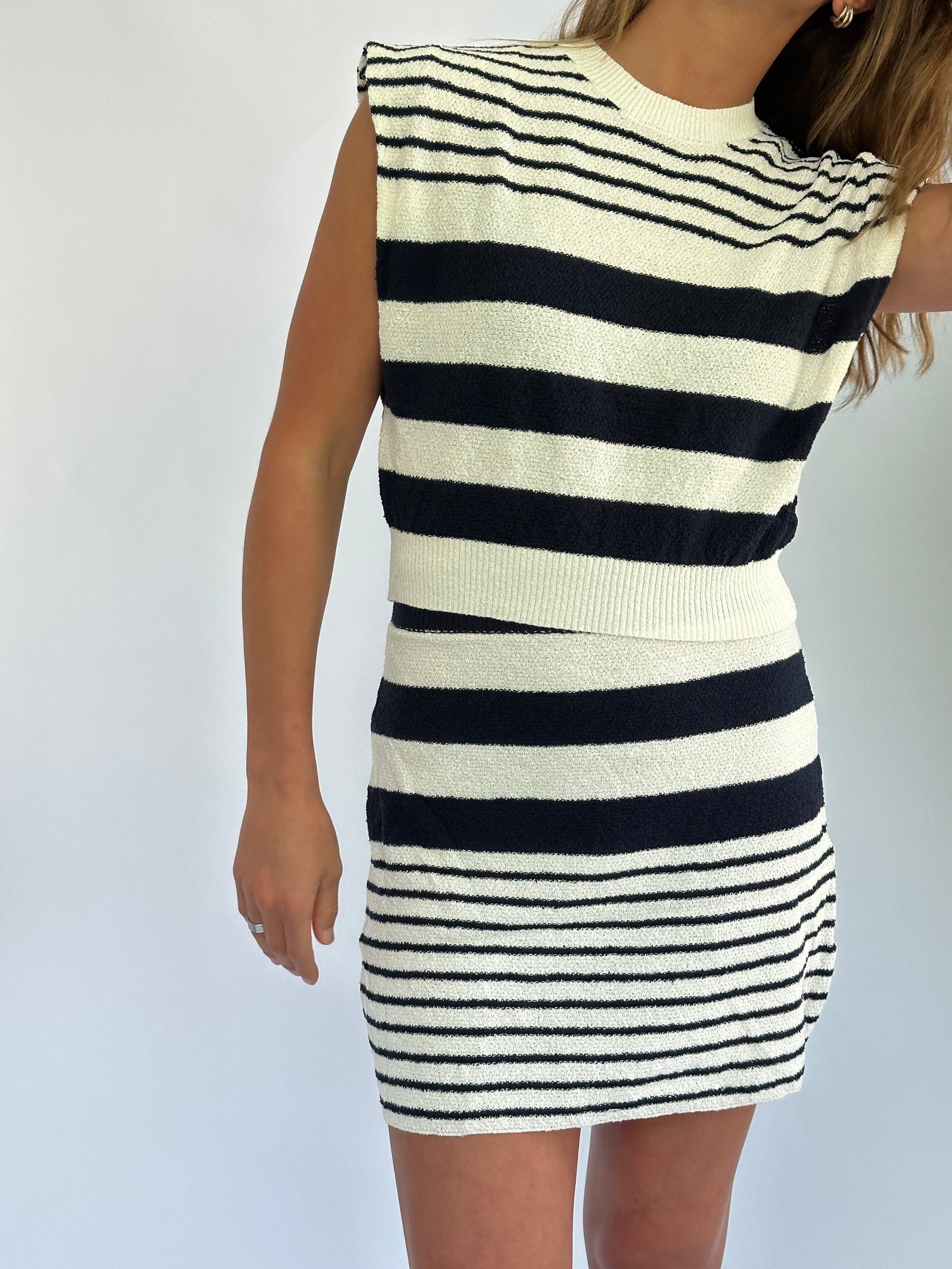 A woman in a sleeveless, black-and-white striped terry set poses against a plain white background. The pattern varies, with wider stripes on top and finer ones on the skirt.
