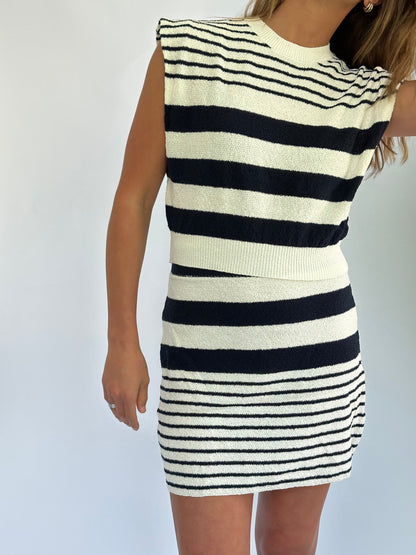 A woman in a sleeveless, black-and-white striped terry set poses against a plain white background. The pattern varies, with wider stripes on top and finer ones on the skirt.