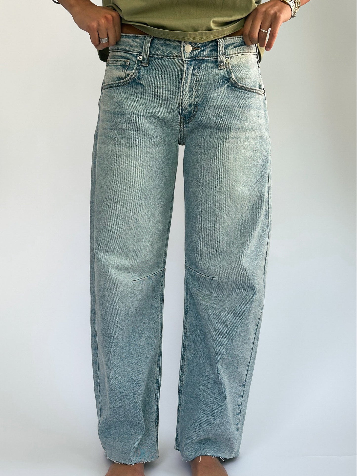 A person wearing light wash wide-leg jeans and a green top. The jeans have a casual, relaxed fit, and the person is accessorized with rings.
