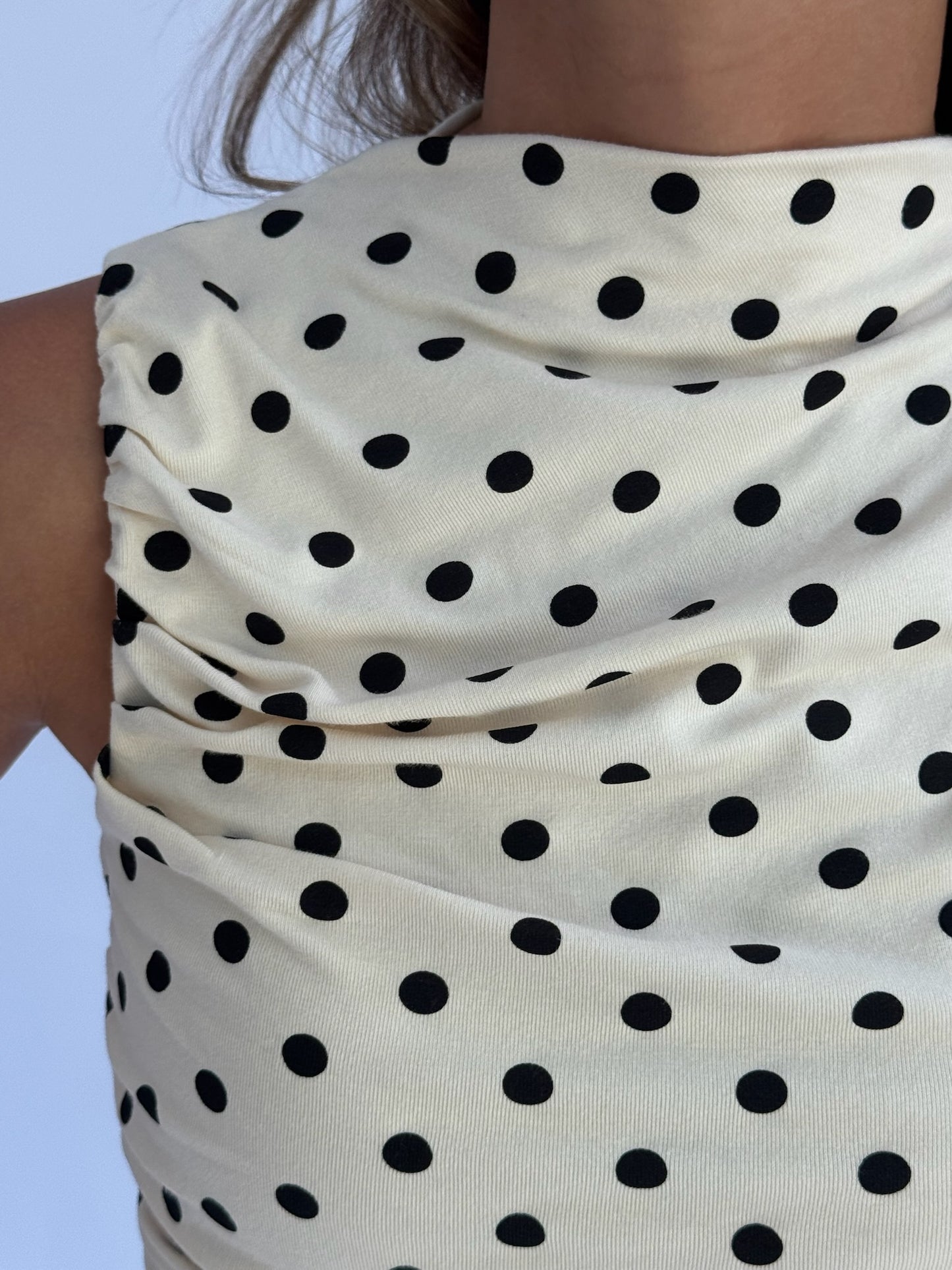 Close-up of a beige sleeveless top with black polka dots, featuring ruched fabric. The setting is neutral, conveying a casual yet stylish tone.