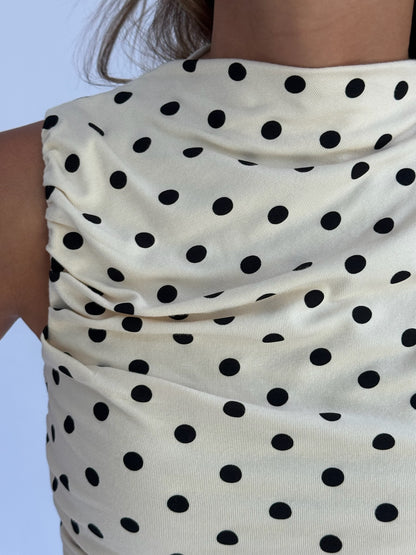 Close-up of a beige sleeveless top with black polka dots, featuring ruched fabric. The setting is neutral, conveying a casual yet stylish tone.