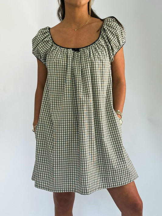 Woman wearing a short-sleeve, checkered dress with a scoop neckline. The dress is loose-fitting and hits above the knees, creating a casual look.