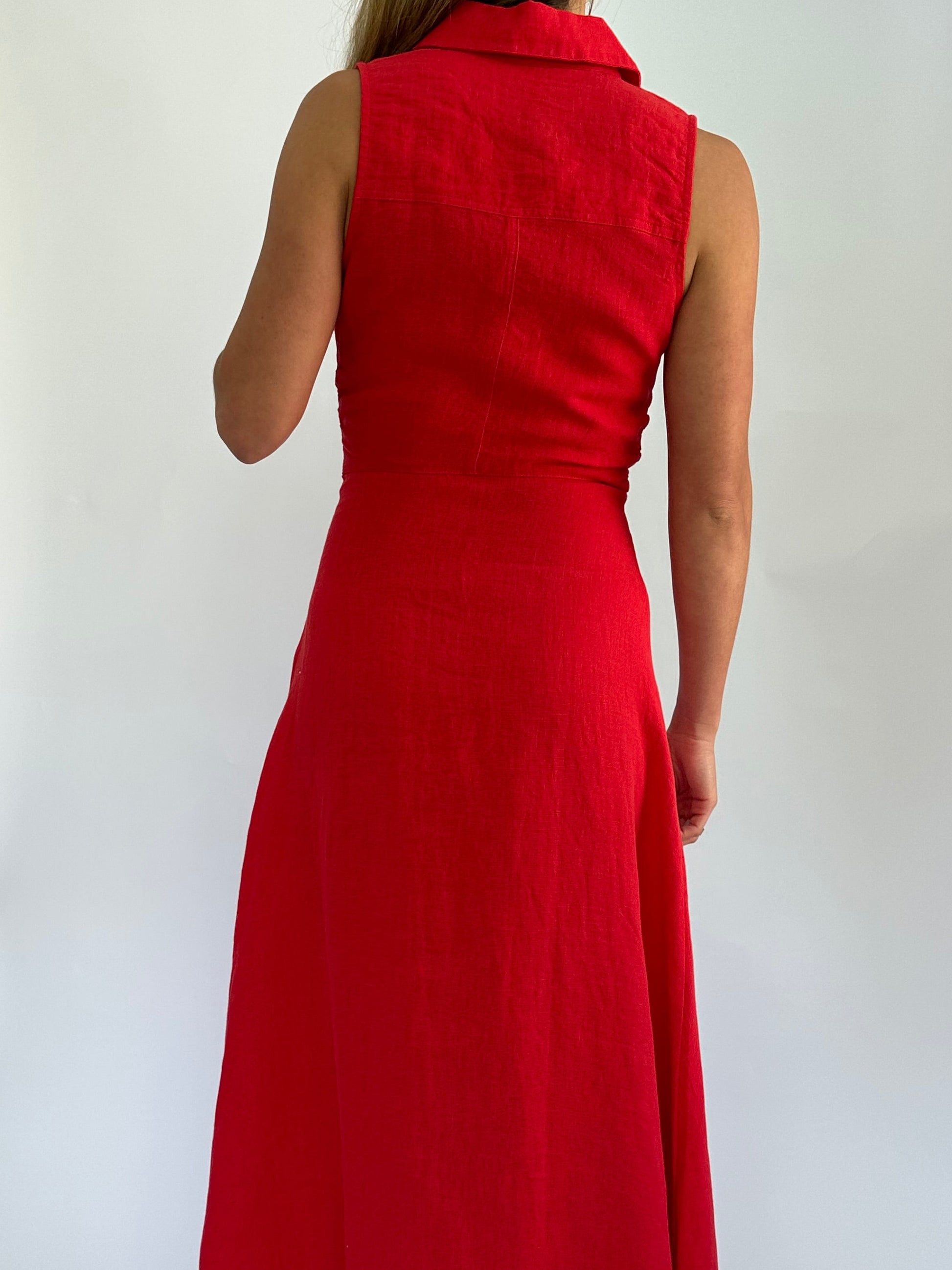 A woman in a sleeveless, knee-length red dress stands with her back to the camera against a plain white background, conveying a simple, elegant style.