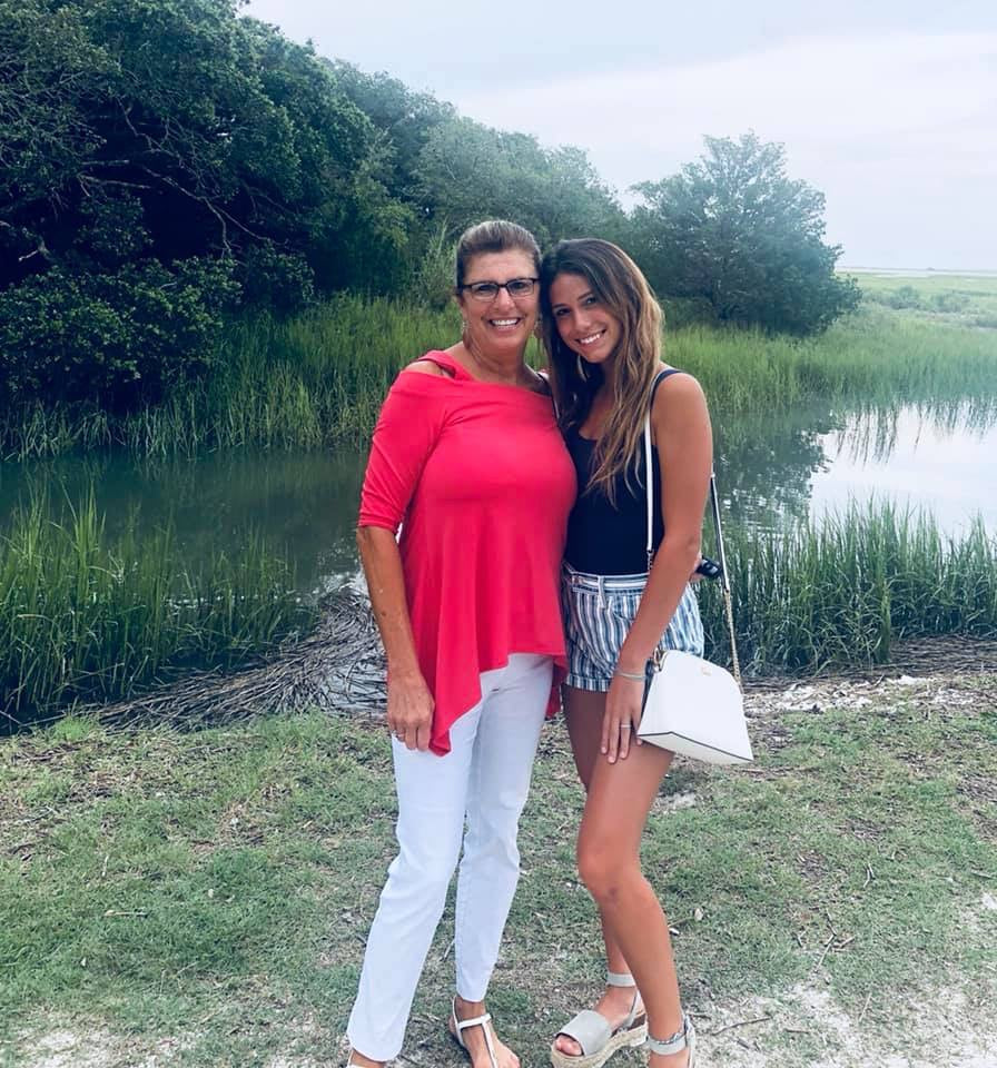 Two women standing by a lake with greenery in the background