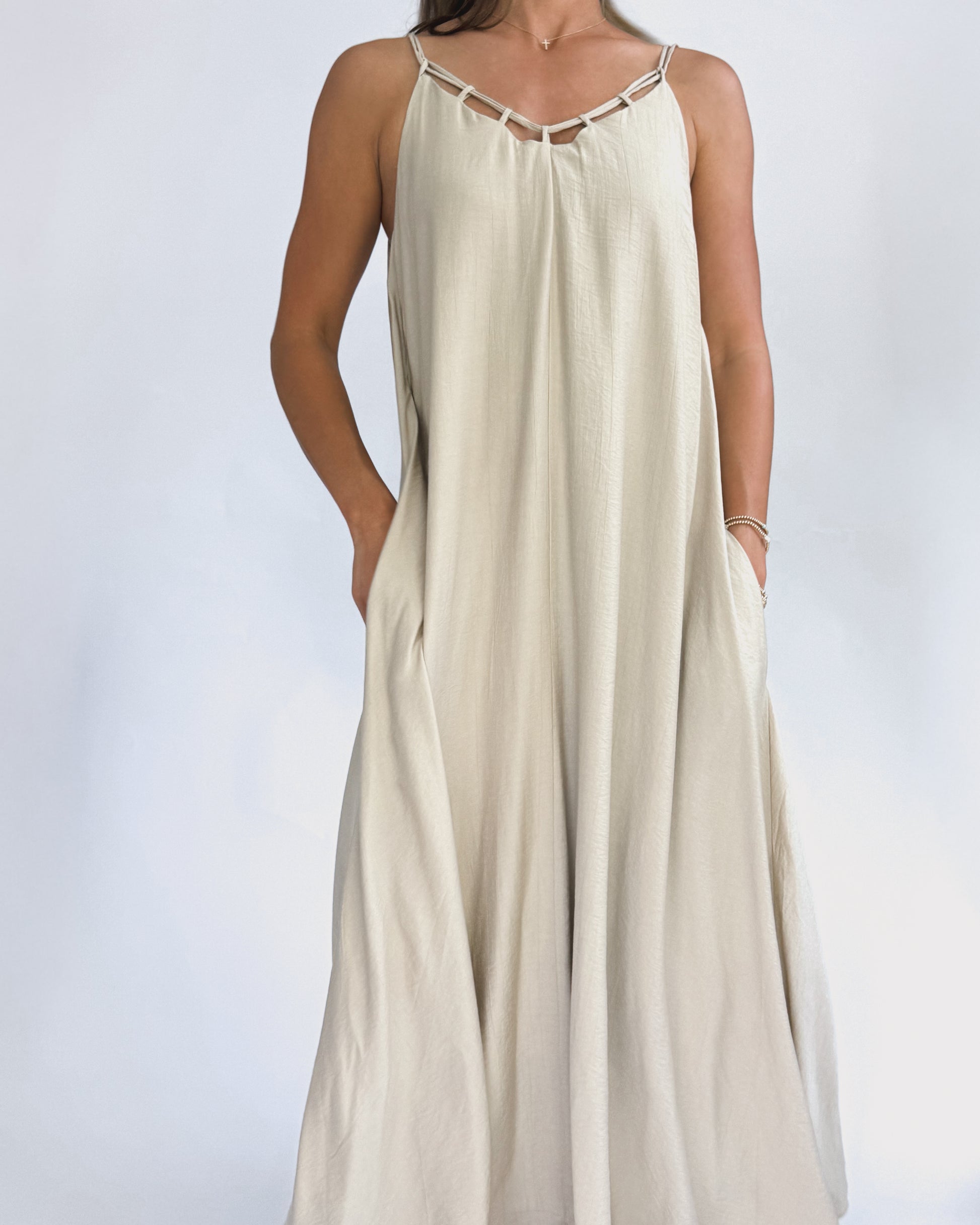 A woman models a flowing, cream maxi dress with a lattice neckline. The lightweight fabric drapes elegantly, creating a relaxed, summery vibe.