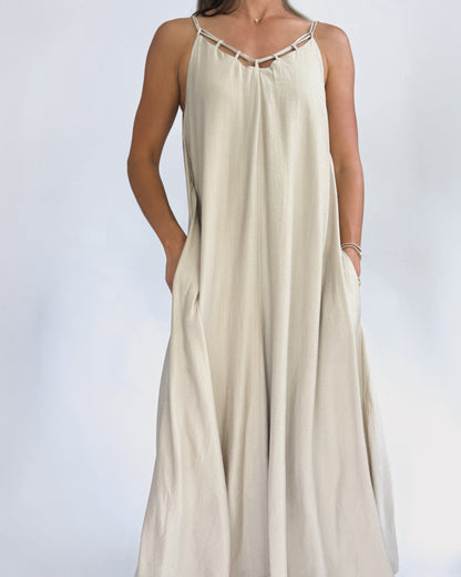 A woman models a flowing, cream maxi dress with a lattice neckline. The lightweight fabric drapes elegantly, creating a relaxed, summery vibe.