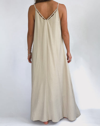 A woman models a flowing, cream maxi dress with a lattice neckline. The lightweight fabric drapes elegantly, creating a relaxed, summery vibe.