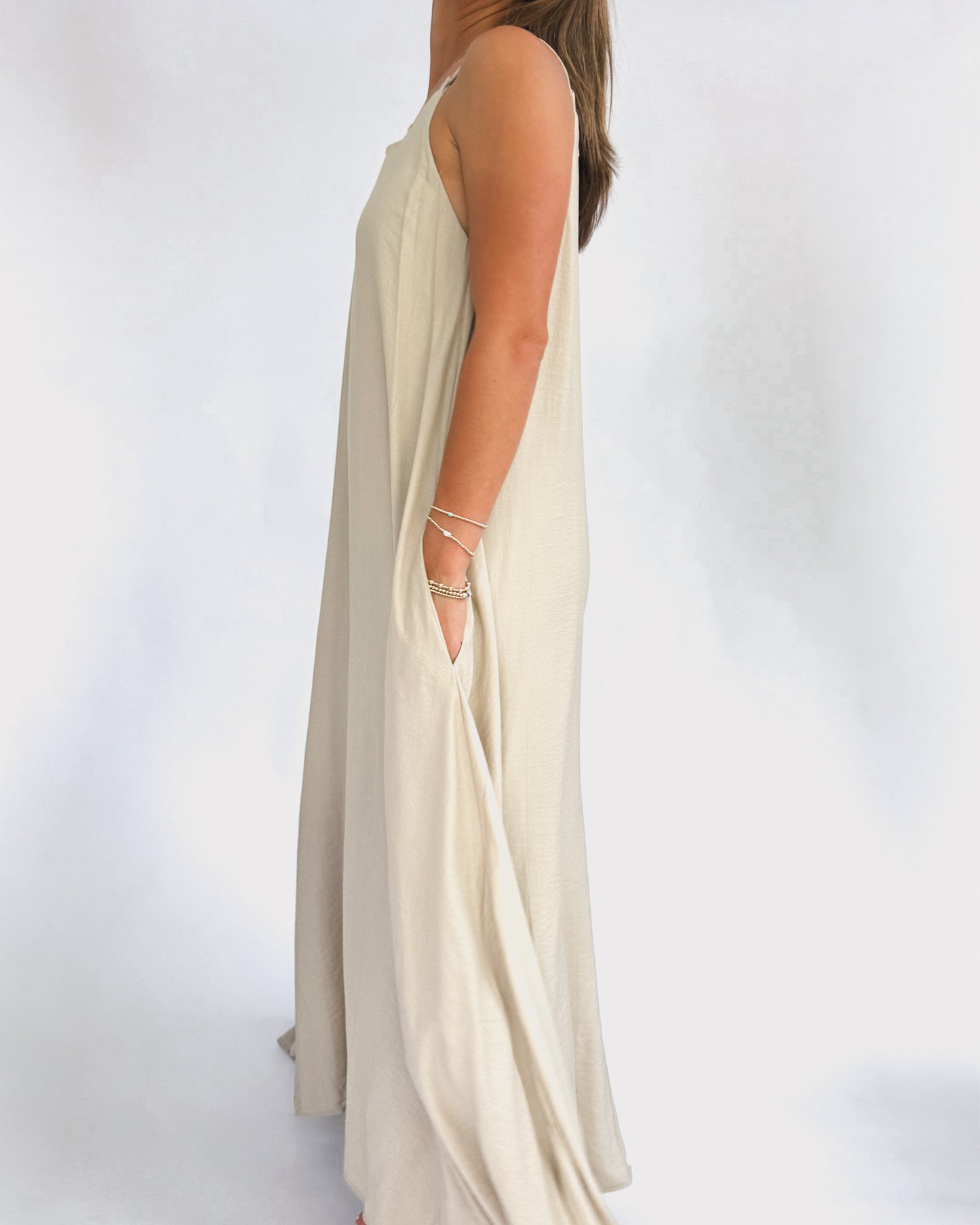 A woman models a flowing, cream maxi dress with a lattice neckline. The lightweight fabric drapes elegantly, creating a relaxed, summery vibe.