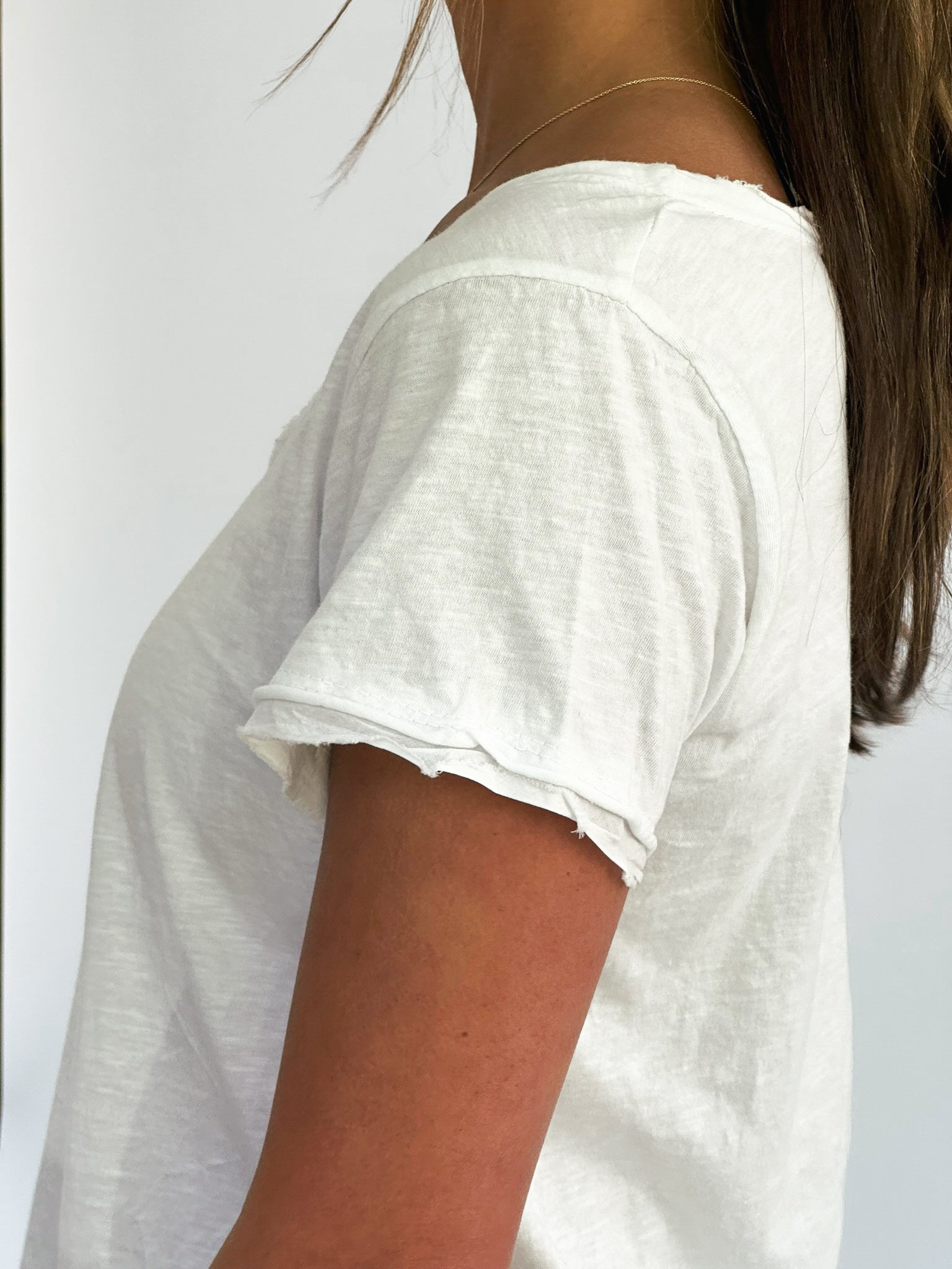 A close-up of a person wearing a white, distressed t-shirt with a frayed sleeve. The background is plain white, creating a minimalistic feel.