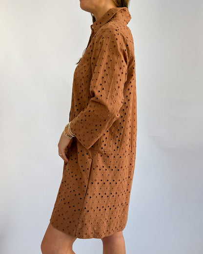 Side view of a woman wearing a brown, long-sleeved dress with black polka dots. The dress has a collared neckline. The tone is casual and relaxed.