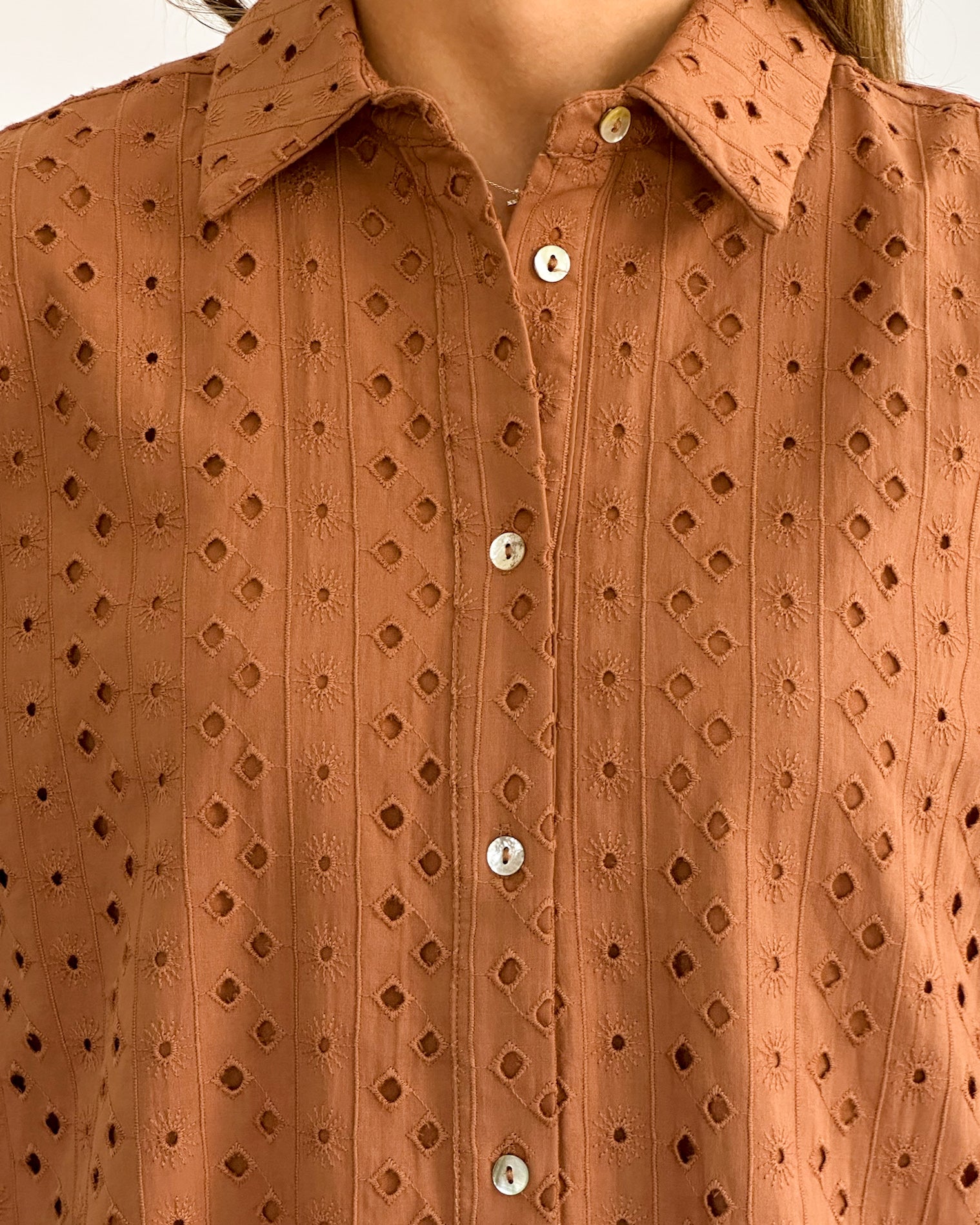 A person in a rust colored, patterned button-up dress with three-quarter sleeves.