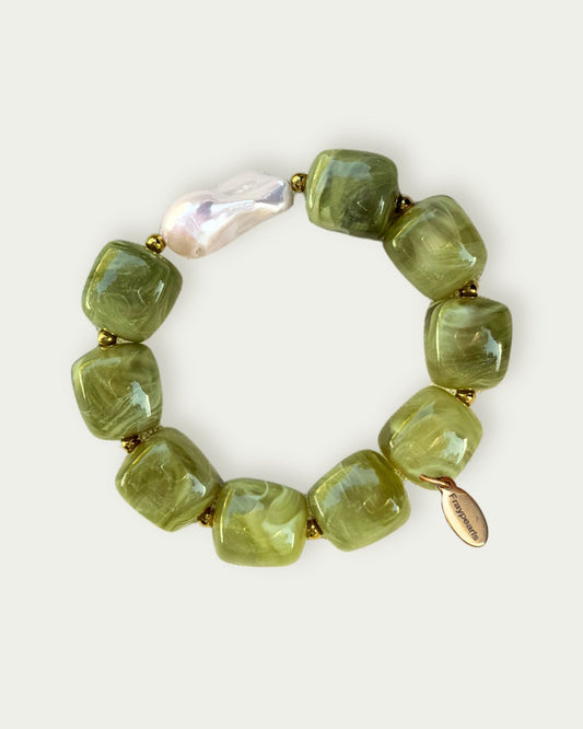 Green bead bracelet with a single cream-colored bead and a small gold tag. The beads have a glossy finish and are connected with small gold spacers.