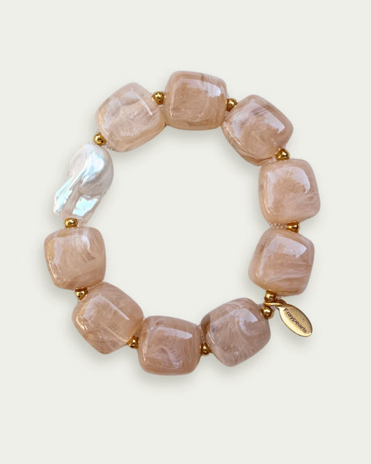 A bracelet made of square, peach-toned stones and small gold beads, featuring an irregular white pearl. The look is elegant and stylish.