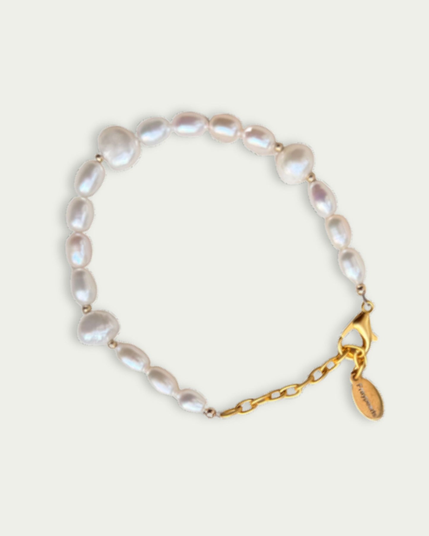 Delicate pearl bracelet with irregular white pearls linked by tiny beads, featuring a gold chain clasp and small engraved gold tag. Elegant and classic.