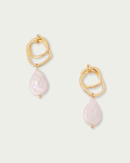 Gold earrings featuring abstract loops and dangling white pearls, set against a plain background, conveying elegance and simplicity.