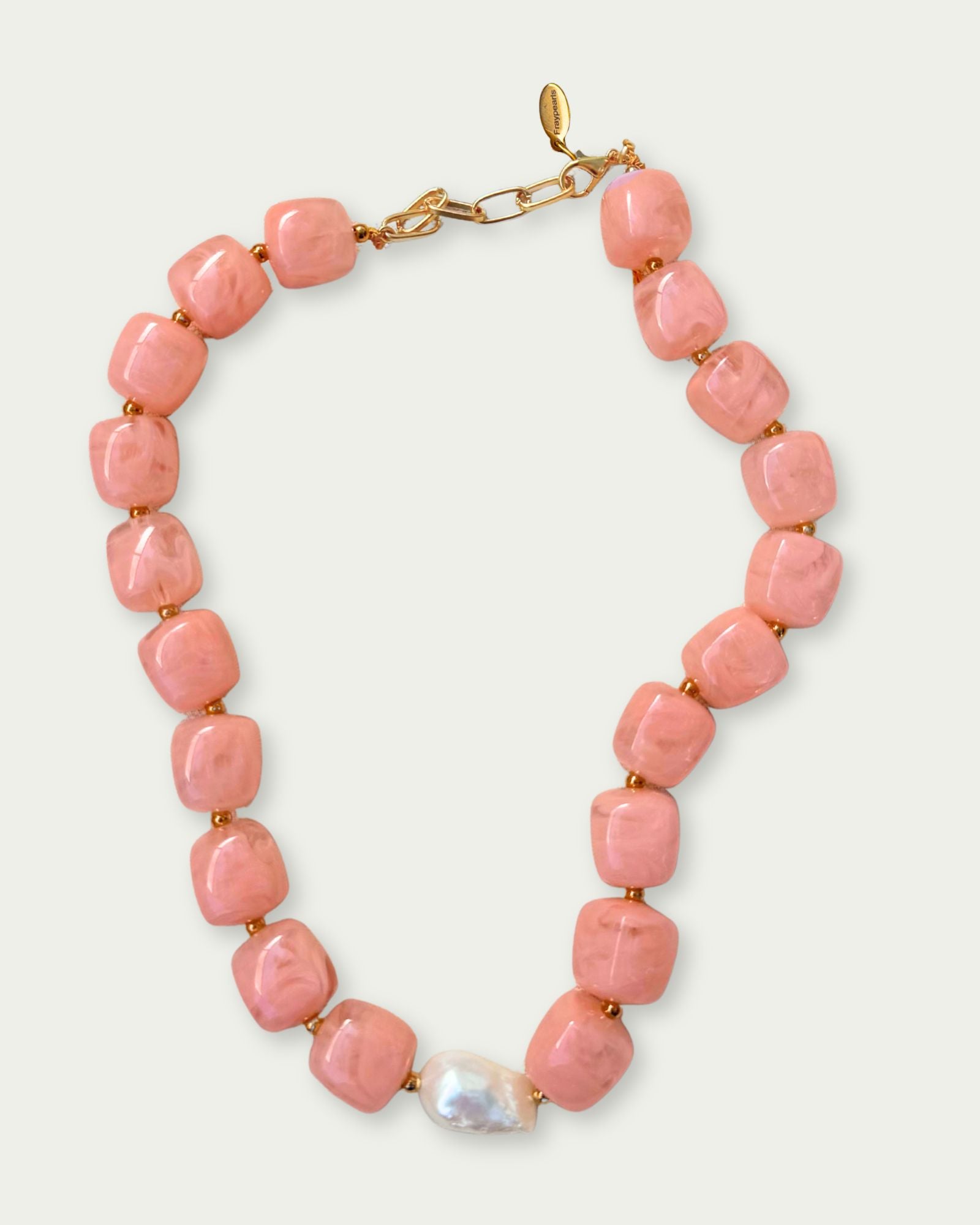 Necklace with pink square beads and small gold accents, featuring a large white irregular bead. Gold clasp. Elegant and stylish design.