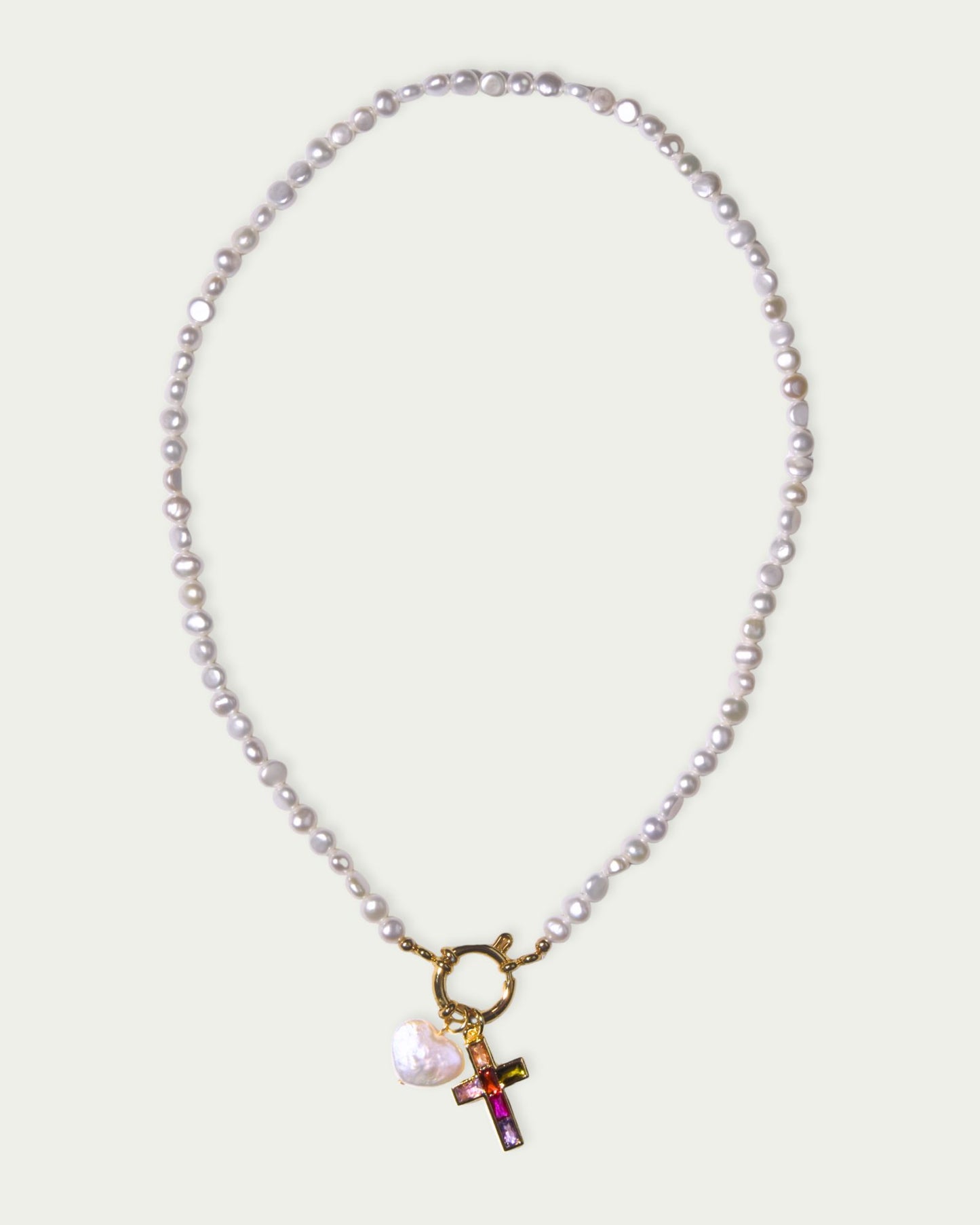 A pearl necklace with a gold clasp features a colorful cross pendant and a white heart charm. The design conveys elegance and modern style.