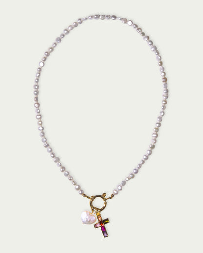 A pearl necklace with a gold clasp features a colorful cross pendant and a white heart charm. The design conveys elegance and modern style.