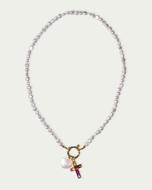 A pearl necklace with a gold clasp features a colorful cross pendant and a white heart charm. The design conveys elegance and modern style.