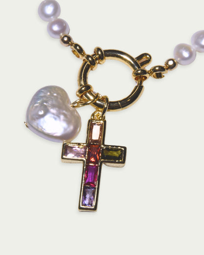 A gold necklace with a heart-shaped pearl and a gemstone cross pendant, featuring vibrant colors. The tone is elegant and sophisticated.