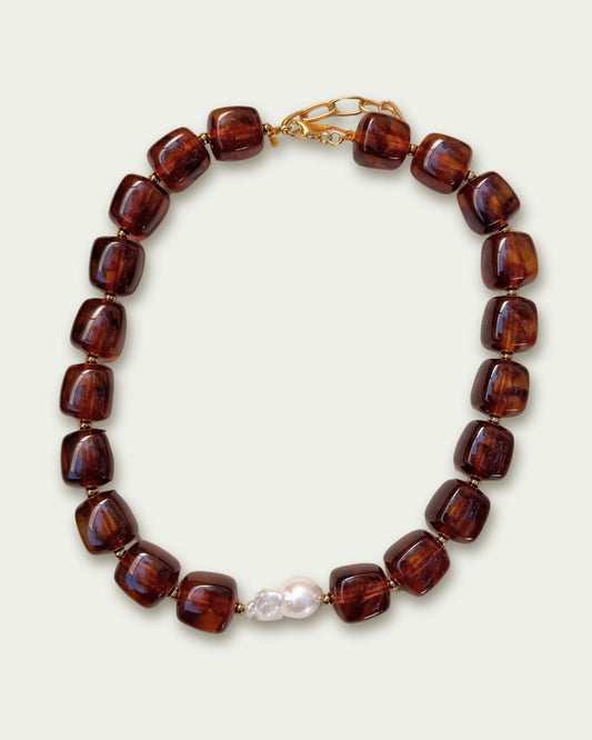 Necklace with polished brown beads arranged in a circular pattern, featuring a standout white pearl at the center and a gold clasp for fastening.