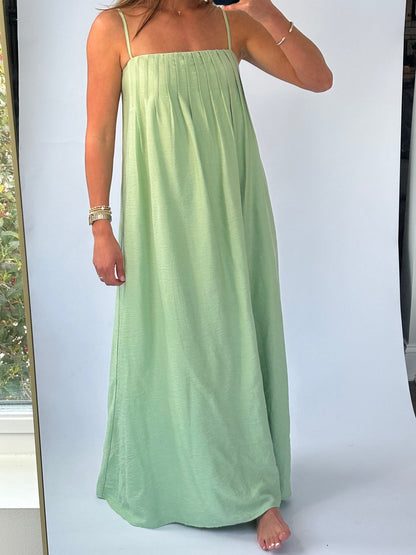 A woman wearing a flowing green sundress with thin straps takes a mirror selfie. She is exuding a relaxed and confident vibe.
