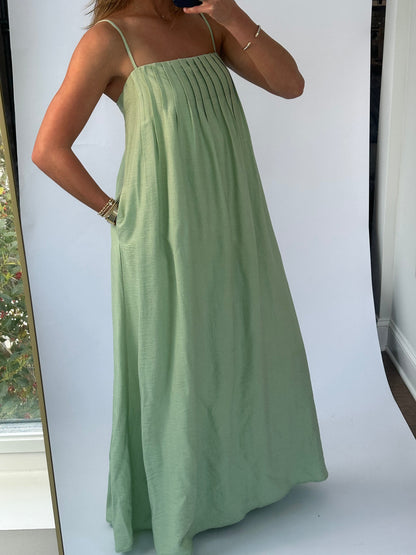 A woman wearing a flowing green sundress with thin straps takes a mirror selfie. 