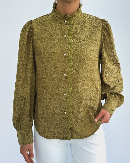 Person wearing a vintage-style green lace blouse with puffed sleeves and pearl buttons, paired with white pants. The look is elegant and classic.