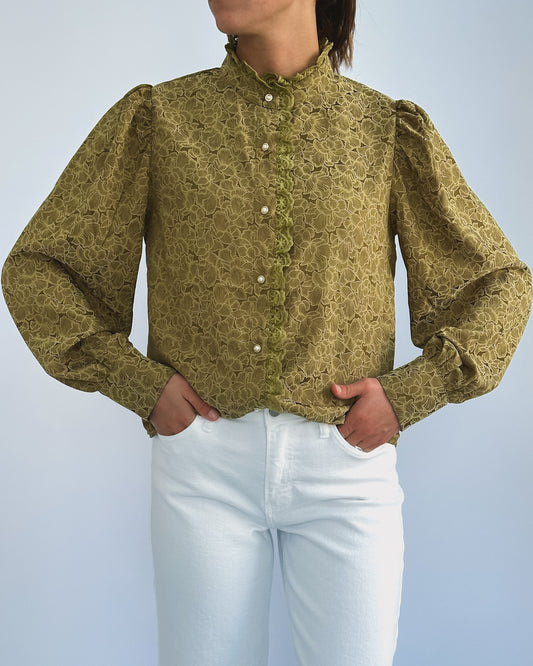 Person wearing a vintage-style green lace blouse with puffed sleeves and pearl buttons, paired with white pants. The look is elegant and classic.