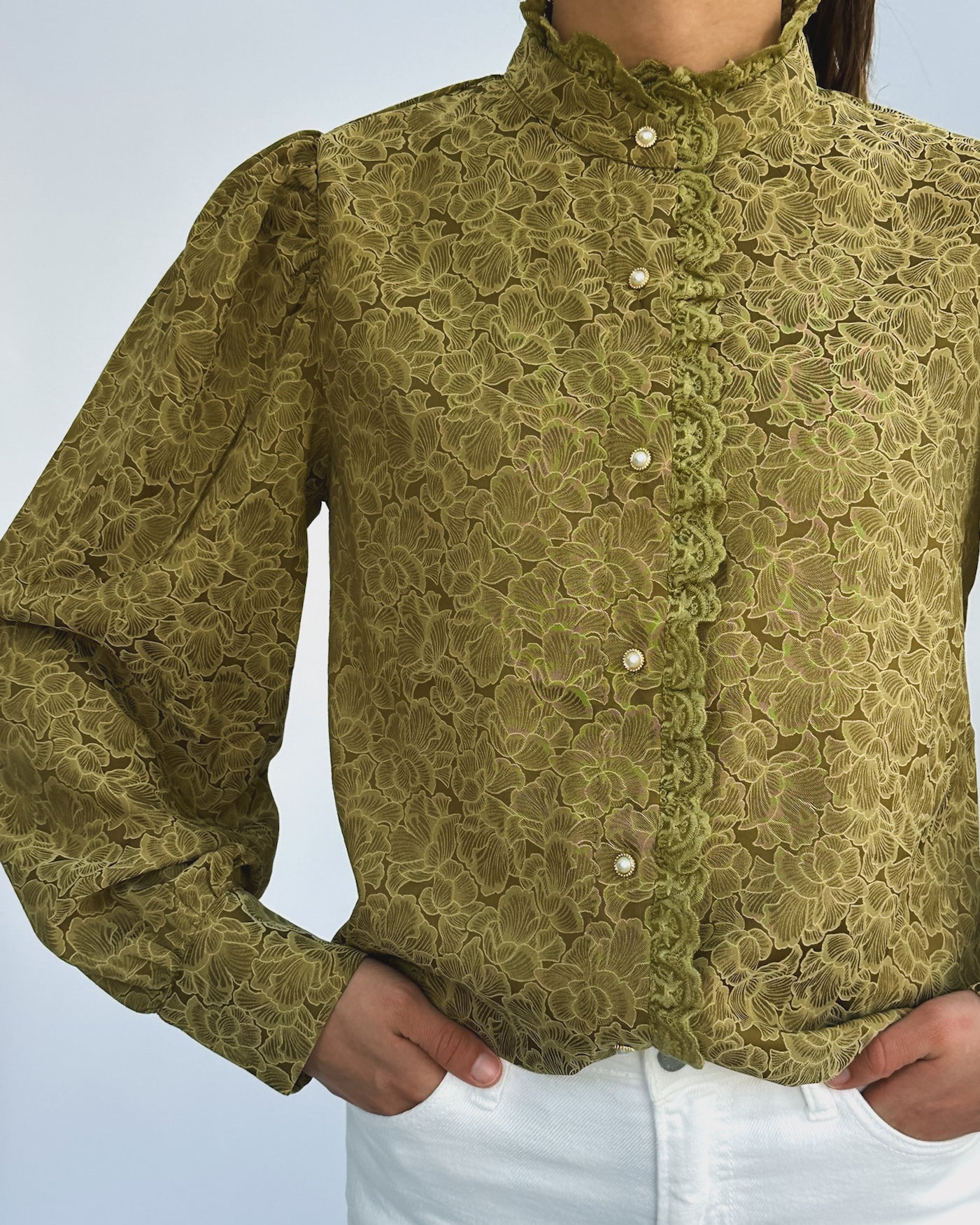 Person wearing a vintage-style green lace blouse with puffed sleeves and pearl buttons, paired with white pants. The look is elegant and classic.