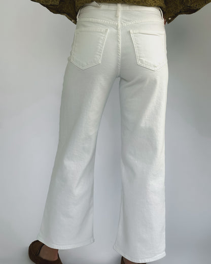 Wide-leg white jeans on a person against a plain background. They wear a green patterned top and brown shoes, creating a casual, stylish look.