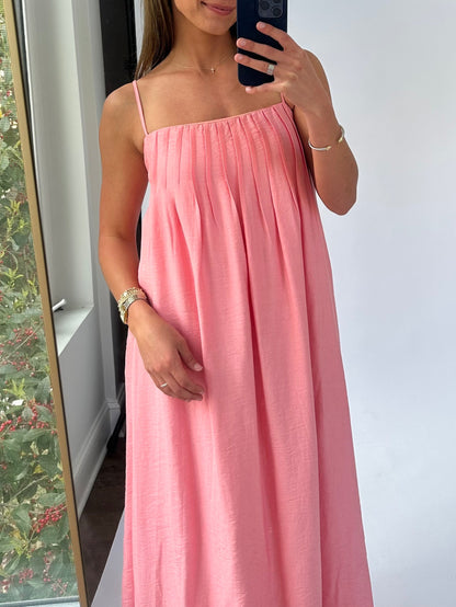 A woman wearing a flowing pink sundress with thin straps takes a mirror selfie. She smiles softly, exuding a relaxed and confident vibe.