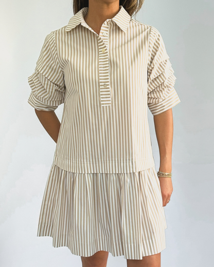 A person wearing a beige and white vertically striped shirtdress with ruffled sleeves. The dress has a collared neckline and falls above the knee.