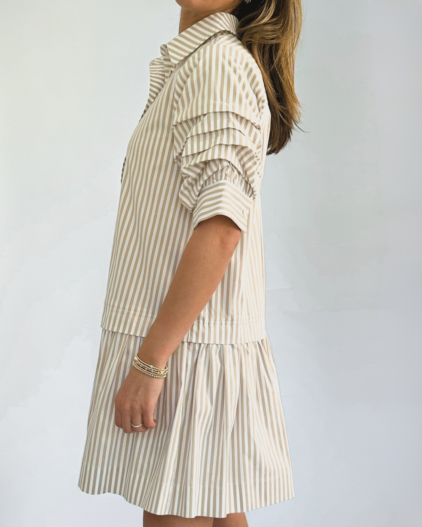 A person wearing a beige and white vertically striped shirtdress with ruffled sleeves. The dress has a collared neckline and falls above the knee.