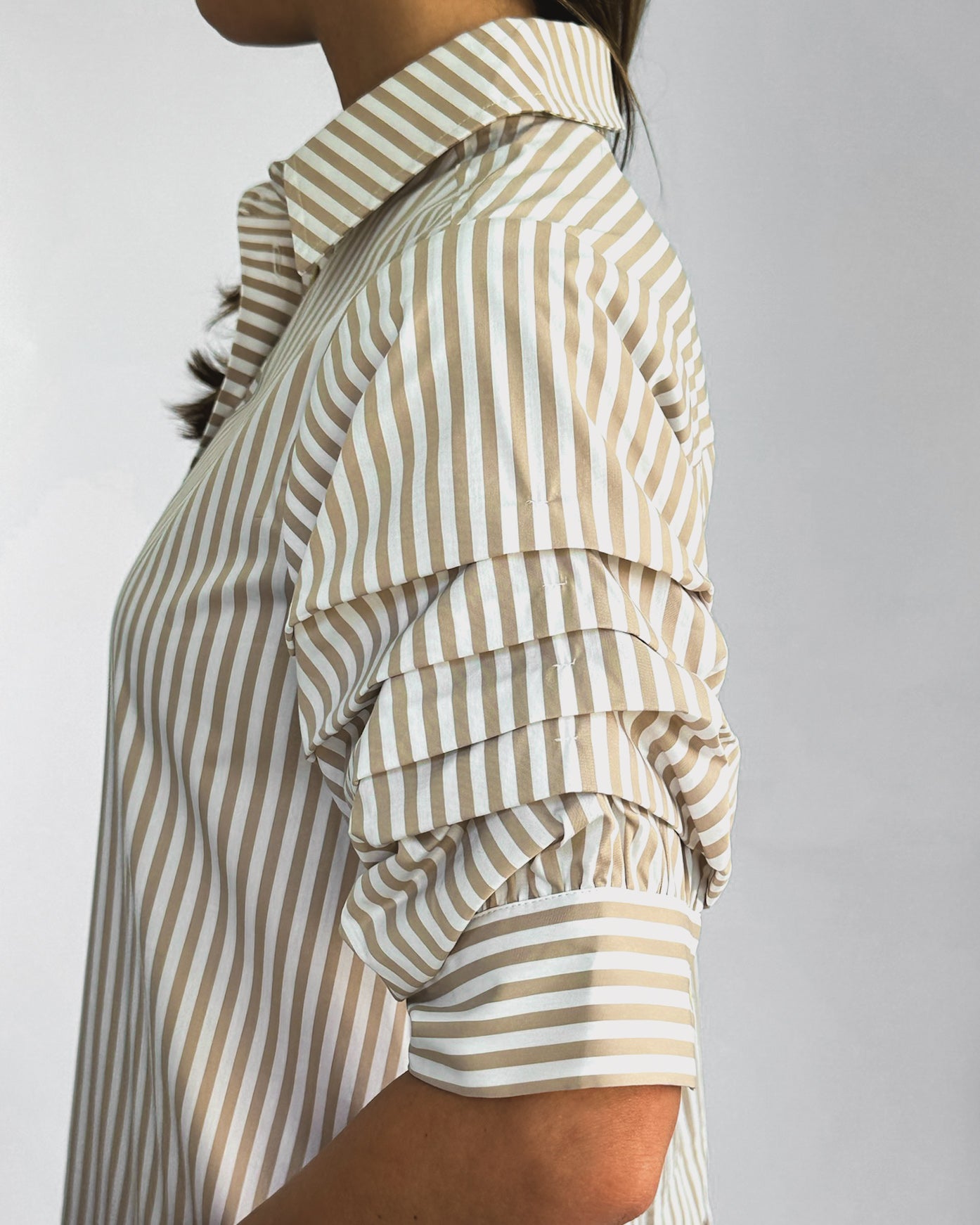 A person wearing a beige and white vertically striped shirtdress with ruffled sleeves. The dress has a collared neckline and falls above the knee.