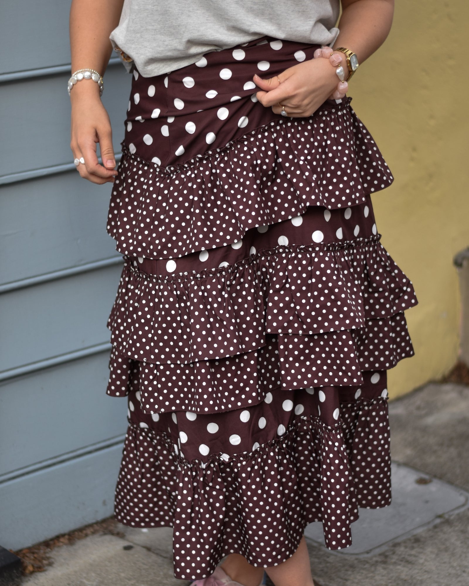A person wearing a brown polka dot tiered skirt with white dots, standing against a blue and yellow background. The mood is casual and stylish.